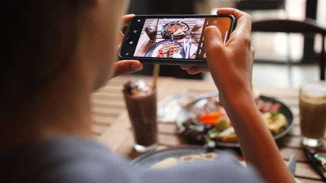 Young Woman Taking Photo of Healthy Breakfast Using Mobile Phone in Vegan Restaurant. 4K Slowmotion Flatlay Food Photography on Wooden Table in American Diner. Thailand.