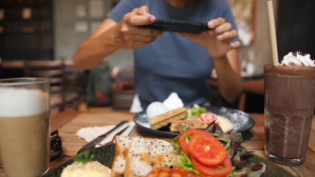 Young Woman Taking Photo of Healthy Breakfast Using Mobile Phone in Vegan Restaurant. 4K Slowmotion Flatlay Food Photography on Wooden Table in American Diner. Thailand.