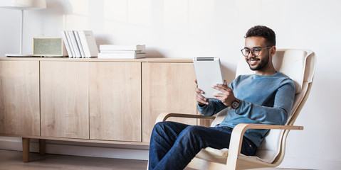 Handsome young man using digital tablet at home. Student men resting in his room. Home work or...