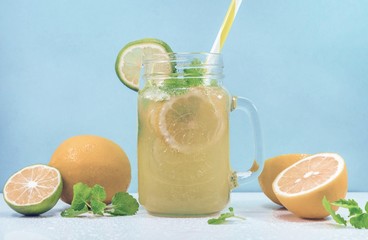 Lemonade drink of soda water, citrus and mint on the light blue background. Cocktail glass with handle and straw, sliced lemon and lime, front view