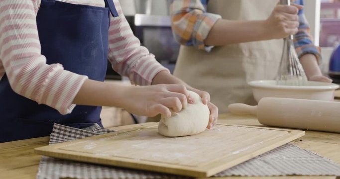unrecognized young asian woman mom in apron holding bowl with dough and whisk in wooden kitchen house. little girl daughter standing beside kneading fresh dough for baking bread pasta pizza to mother