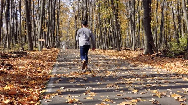 a man climbs on a longboard uphill on the asphalt covered with leaves