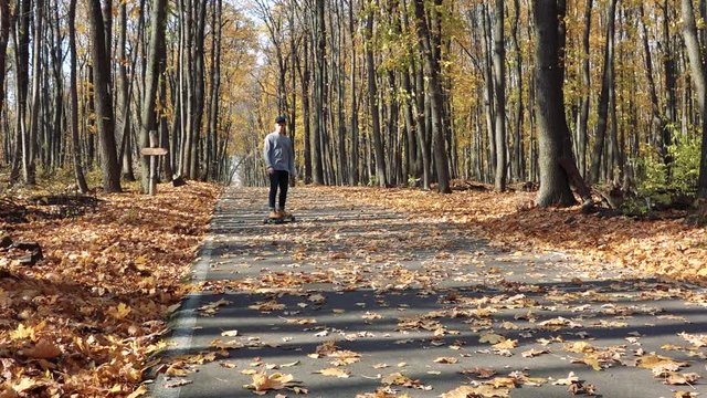a man descends on a longboard uphill on asphalt covered with leaves