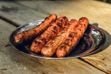 Sausages cooking on grill served on a plate. Food background with barbecue party, front view