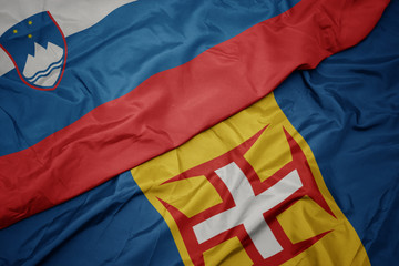 waving colorful flag of madeira and national flag of slovenia.