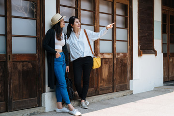 Young attractive asian chinese woman pointing finger showing friend with blue sunny sky. Portrait of two gorgeous girls travel in summer time in tokyo japan. full length sisters enjoy view outdoor