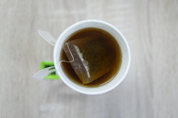 Top view of a paper cup of tea with tea bag on wooden background.