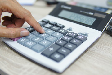Male hand press the button of calculator to calculate and analyze the data at office desk.