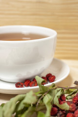 White cup of tea with plate and dry rowan berries wooden background vertical detailed
