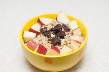 A healthy breakfast of oatmeal cooked in milk with apples and chocolate with nuts in a yellow plate.