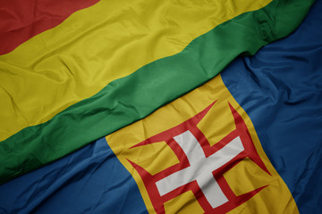 waving colorful flag of madeira and national flag of bolivia.