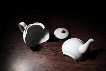 broken teapot on a dark toned foggy background. Pieces of ceramic teapot on wooden table.