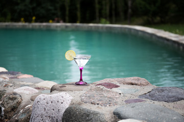 Glass of martini cocktail at swimming pool with ocean and palm tree background. A glass of blue martini cocktail welcome drink bar.Selective focus. season and holidays concept.