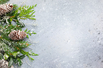 Christmas or winter background with a border of green and frosted evergreen branches and pine cones on a grey vintage board. Flat lay