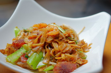 Penang Char Kway Teow or Char Koay Teow (stir-fried rice cake strips / fried flat noodles) in white plate at Southeast Asia cuisine restaurant