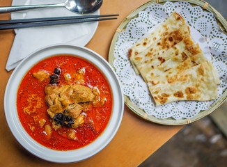 Red chicken curry with anise in ceramic bowl and fried flatbread in round bamboo plate with chopsticks and spoon on yellow table top view