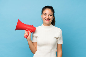 Young brunette girl over isolated blue background holding a megaphone