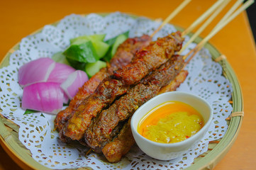 Satay chicken and beef skewers with sliced onion and cucumber on paper mat and bamboo plate at at Southeast Asia cuisine restaurant