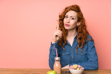 Redhead woman having breakfast cereals and fruit pointing with the index finger a great idea