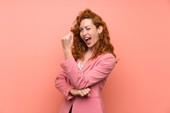 Redhead woman in suit over isolated pink wall making strong gesture