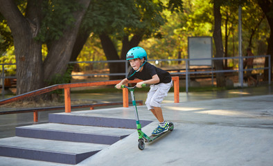 A boy on a scooter and in protective helmet do incredible stunts in skate park. Extreme jump. The concept of a healthy lifestyle and sports leisure - obrazy, fototapety, plakaty
