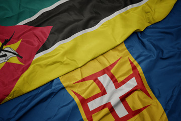 waving colorful flag of madeira and national flag of mozambique.