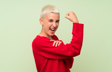 Teenager girl with white short hair over green wall doing strong gesture
