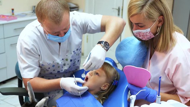 A girl is sitting in a dental chair. The dentist and his assistant treat the teeth of a child in a dental clinic.