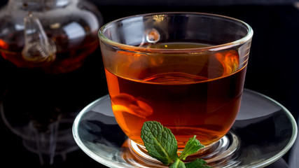 Cup of tea with a leaf of mint on a black background