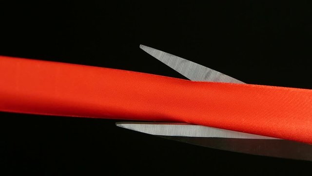 On a black background cut red ribbon scissors. Slow motion
