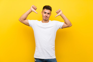 Young handsome man over isolated yellow background showing thumb down