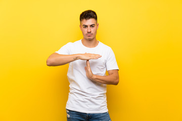 Fototapeta na wymiar Young handsome man over isolated yellow background making time out gesture