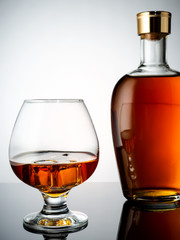 A glass of cognac and a filled bottle of cognac on a wooden background