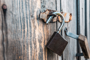 An open padlock hanging on the gate of an old village barn