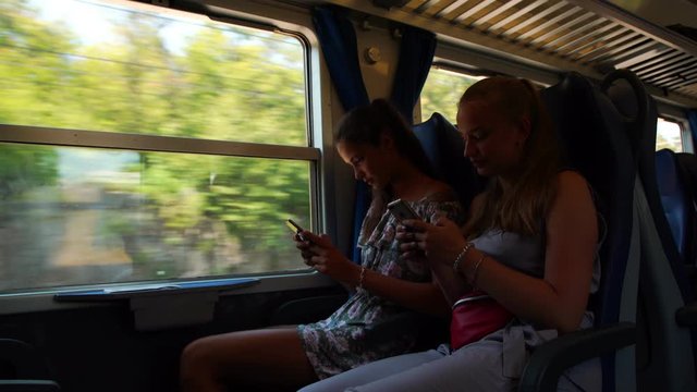 young girls sit next to each other and share cool pictures on phone passing beautiful landscapes in intercity train