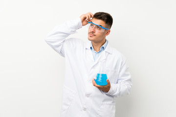 Young scientific holding laboratory flask over isolated background having doubts and with confuse face expression