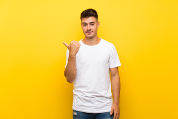 Young handsome man over isolated yellow background pointing to the side to present a product