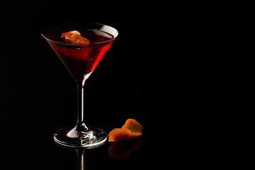 Cosmopolitan cocktail in nice red color in front of a black background, served with orange peel. Space for text, copy paste