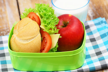 Healthy school lunchbox containing roll with cheese, lettuce and tomato, red apple glass of milk
