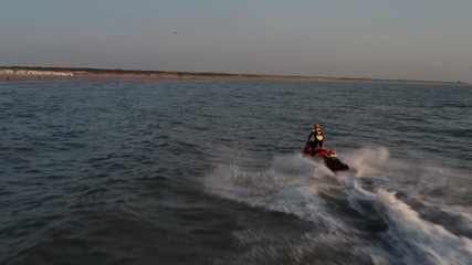 Rescue brigade jetski with a lifeguard hanging on moving fast through sea