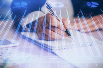 A woman hands writing information about stock market in notepad. Forex chart holograms in front. Concept of research. Multi exposure
