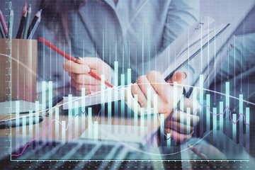 A woman hands writing information about stock market in notepad. Forex chart holograms in front. Concept of research. Multi exposure