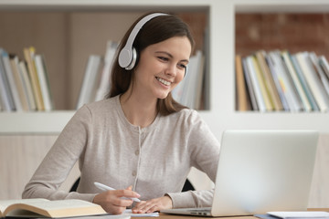 Girl in headphones look at pc screen noting studying indoors