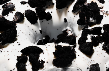 Macro shot donut or doughnut with white frosting and black crumbled cookie topping.