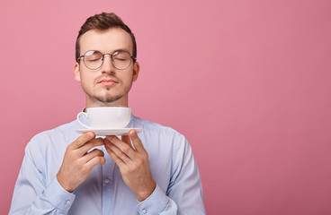 A cheerful responsive student in a light shirt with glasses and a black rim is resting with cup of...