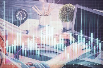 Double exposure of stock graph with businessman typing on computer in office on background. Concept of hard work.