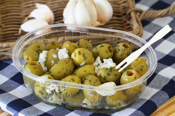 Green olives with garlic in transparent plastic box on checkered cloth