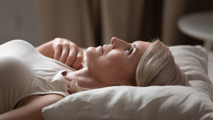 Disturbed mature older woman lying awake in uncomfortable bed