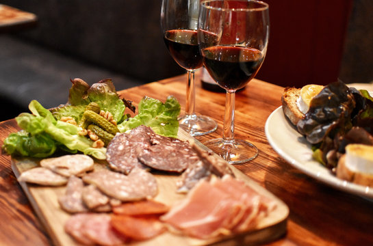 Spanish tapas meal with prosciutto, salami and other cold cuts, salad, pickles, chèvre cheese roasts and red wine. All displayed on wooden table -Image