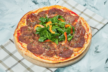 Italian juicy homemade pizza with vitello tonato veal and spinach leaves with red sauce and mozzarella on grey background.